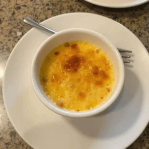 Crab Brulee topped with a golden caramelized sugar crust served in a ramekin with fresh herbs garnish.