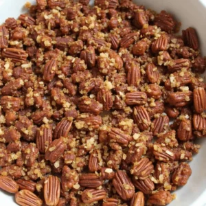 A close-up image of freshly baked spicy bourbon pecans, golden-brown and glistening with a sticky glaze, placed on a baking tray.