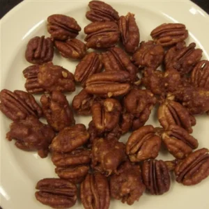Close-up image of spicy bourbon pecans on a rustic wooden table, showing the glistening glaze and crunchy texture.