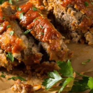 A golden-brown, glazed one-pan meatloaf fresh out of the oven, garnished with parsley and served with mashed potatoes and roasted vegetables on a rustic plate.