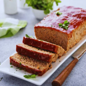 Sliced homemade meatloaf with a caramelized glaze, served with mashed potatoes and green beans