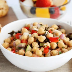 Close-up of a bowl of dense bean salad featuring colorful beans, avocado, cherry tomatoes, and a fresh lemon dressing