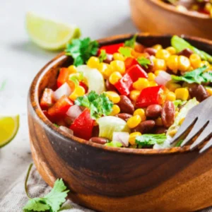 A vibrant bowl of dense bean salad filled with kidney beans, chickpeas, black beans, diced vegetables, and fresh herbs, drizzled with a zesty dressing.