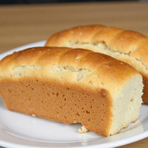 A sliced loaf of Cheesecake Factory brown bread on a wooden cutting board, with butter and honey drizzled on the side.
