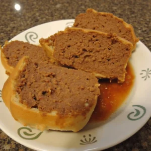 A raw meatloaf mixture in a loaf pan, ready to be baked, with a brush applying a thick layer of ketchup glaze on top.