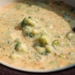 A rustic bowl of thick, creamy Broccoli Cauliflower Cheese Soup topped with shredded cheddar cheese and a sprig of fresh parsley.