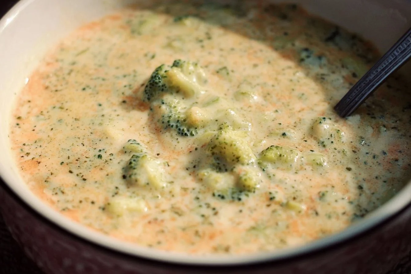 A rustic bowl of thick, creamy Broccoli Cauliflower Cheese Soup topped with shredded cheddar cheese and a sprig of fresh parsley.
