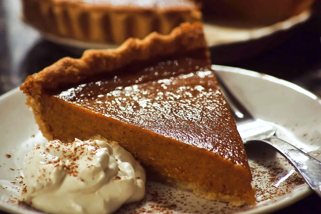 Delicious homemade Pumpkin Pie topped with whipped cream on a rustic table.