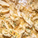 Crockpot chicken and gravy served on a plate with mashed potatoes.