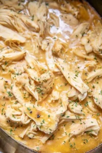 Crockpot chicken and gravy served on a plate with mashed potatoes.
