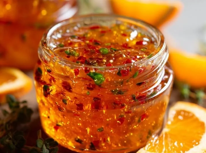 A jar of vibrant Citrus Jelly with slices of oranges and lemons, showcasing its bold color.