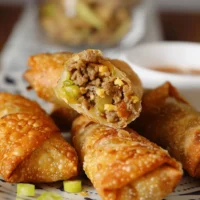 Plate of golden crispy egg rolls served with dipping sauce