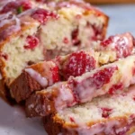 Glazed strawberry bread sliced on a wooden table with fresh strawberries