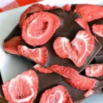 Delicious dark chocolate bark topped with fresh strawberries on a wooden board.