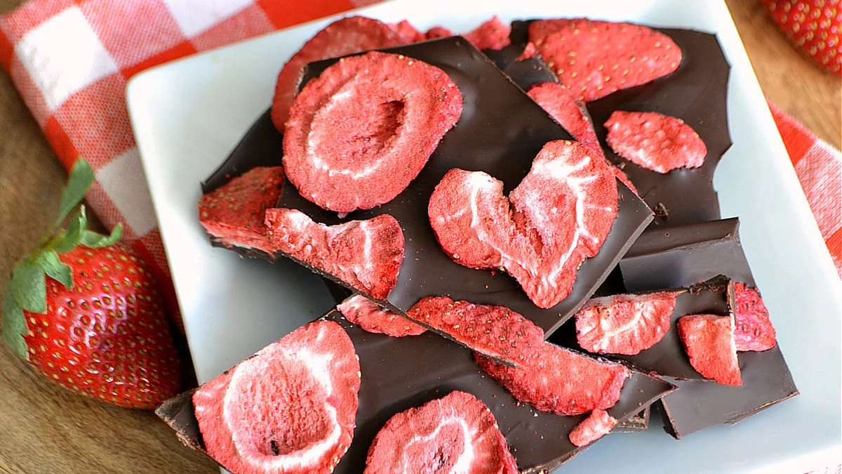 Delicious dark chocolate bark topped with fresh strawberries on a wooden board.